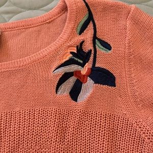 Peach knit sweater with floral embroidery and bell sleeves and hem.